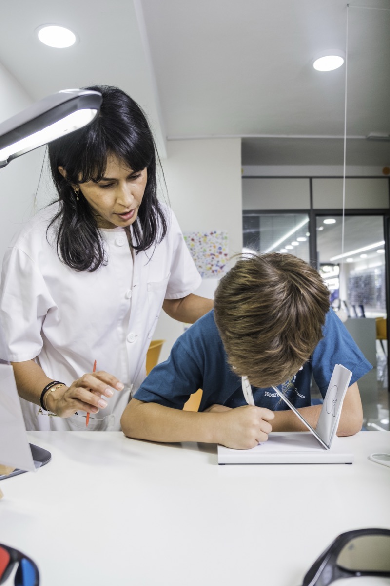 Niño realizando un ejercicio de terapia visual sobre la mesa junto a la optometrista