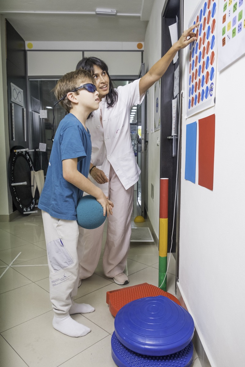 Niño con gafas de anaglifo y balón de equilibrio durante un ejercicio de terapia visual en pared
